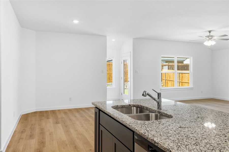 Kitchen with light wood-style flooring, ceiling fan, light stone countertops, dark cabinets, and recessed lighting