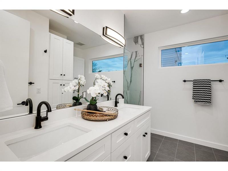 The ensuite primary bathroom offers sleek double sinks, chic gray slate tile, and a spacious walk-in shower.