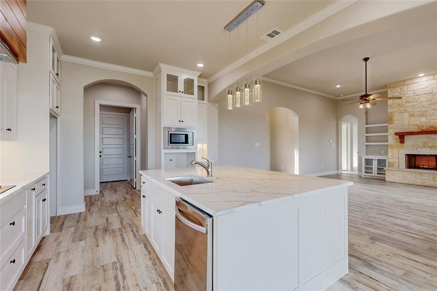 Kitchen featuring a stone fireplace, a center island with sink, sink, decorative light fixtures, and white cabinetry