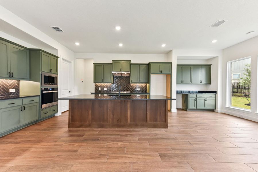 Kitchen with green cabinetry, appliances with stainless steel finishes, backsplash, light wood-style flooring, and recessed lighting