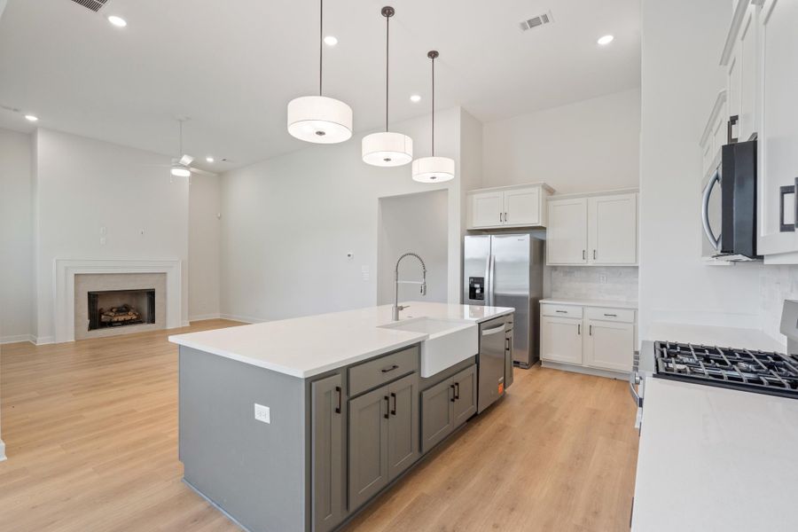 Spacious kitchen island with an undermount farmhouse sink, light wood-finish flooring, and stainless steel appliances, including a range and refrigerator
