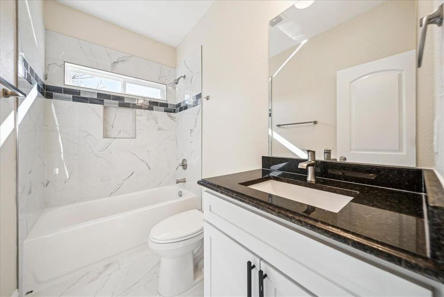 Full bathroom with tiled shower / bath combo, toilet, and vanity