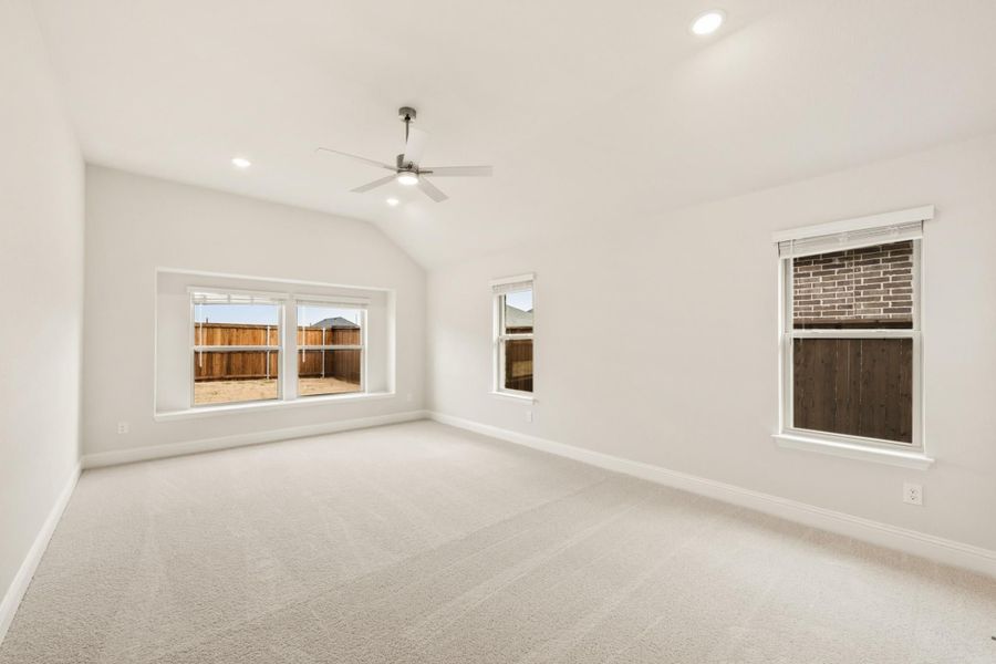 Empty bedroom with vaulted ceiling, ceiling fan, carpet flooring, and three windows with backyard view Empty bedroom with vaulted ceiling, ceiling fan, carpet flooring, and three windows with backyard view