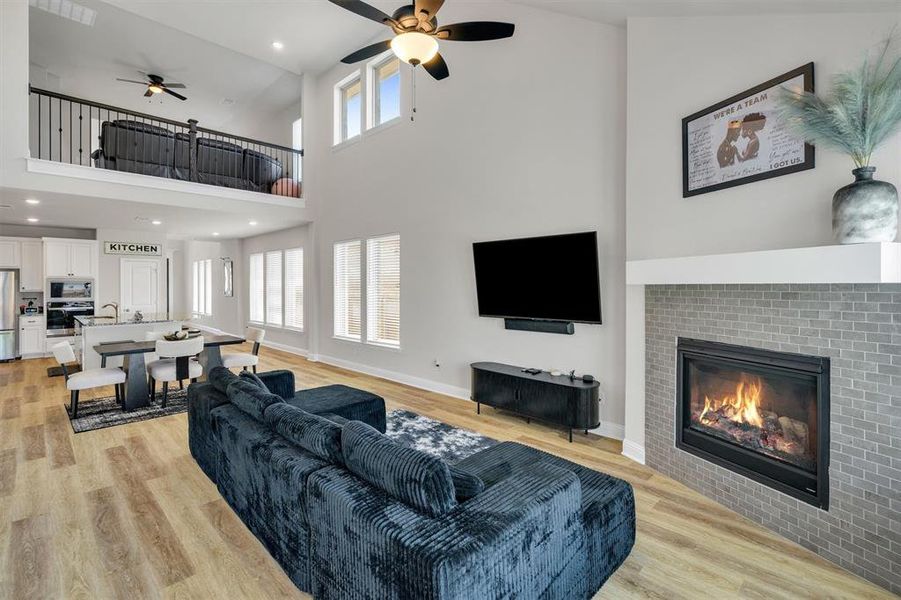 Open-concept living space featuring high ceilings, wood-finish flooring, a fireplace with a light gray tile surround and white mantel, and a kitchen with white cabinetry and an island with seating