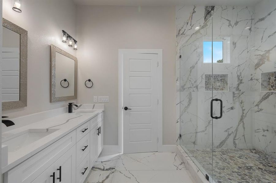 Full bathroom with a marble finish shower, marble finish flooring, double vanity, and baseboards