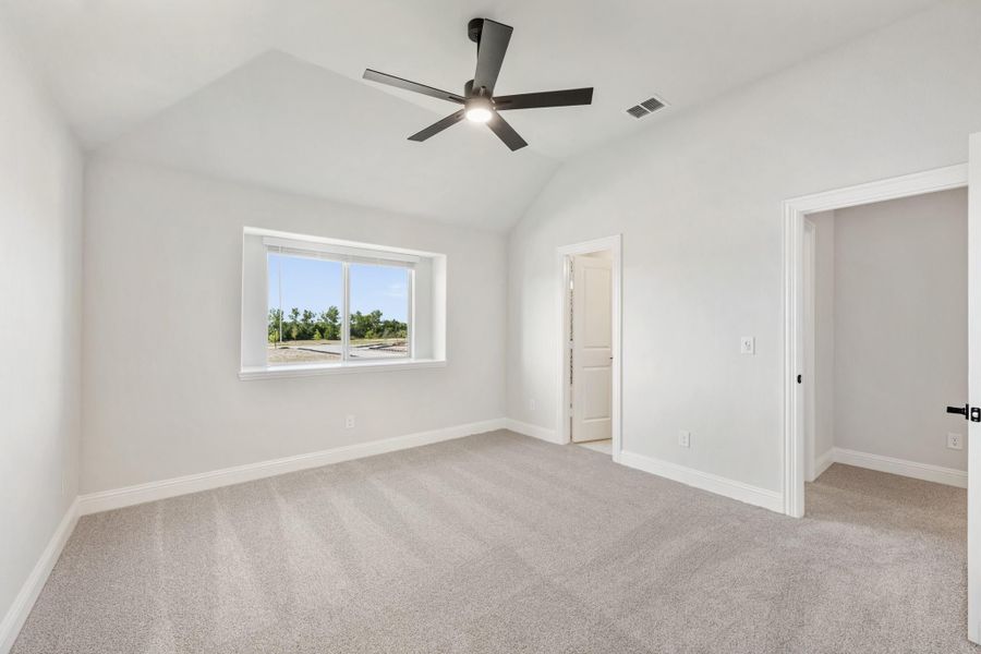 Empty bedroom with vaulted ceiling, ceiling fan, carpet flooring, and two doorways Empty bedroom with vaulted ceiling, ceiling fan, carpet flooring, and two doorways