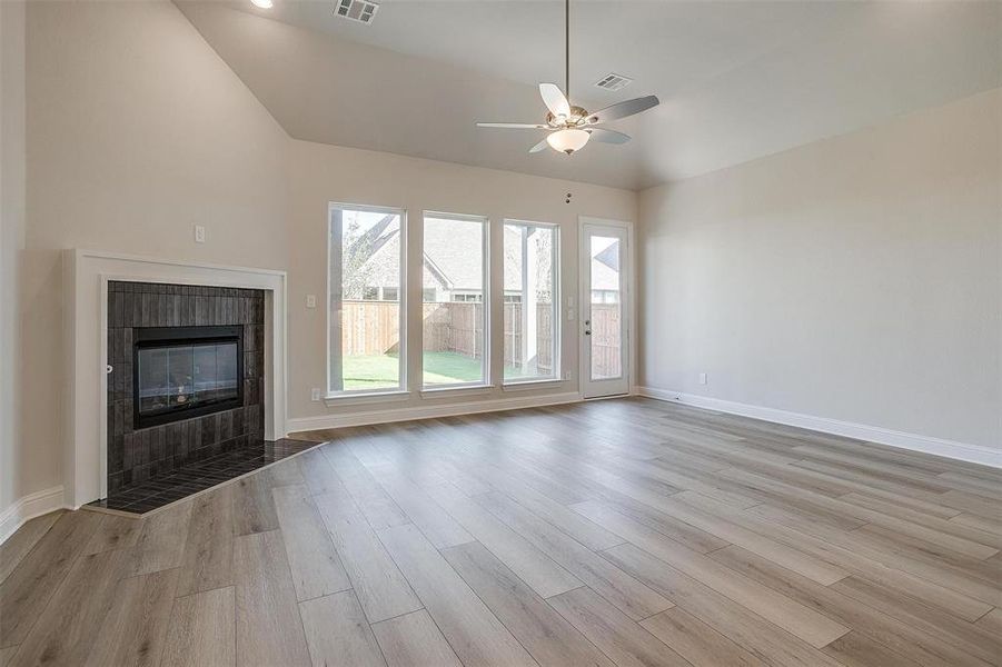 Unfurnished living room with ceiling fan, a fireplace, lofted ceiling, and light wood-type flooring