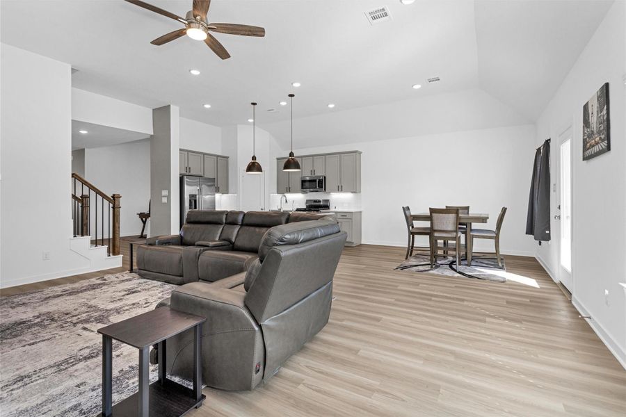 This spacious open-concept living area seamlessly connects the family room, kitchen, and dining area, featuring sloped ceilings, recessed lighting, and natural light—perfect for everyday living and entertaining.