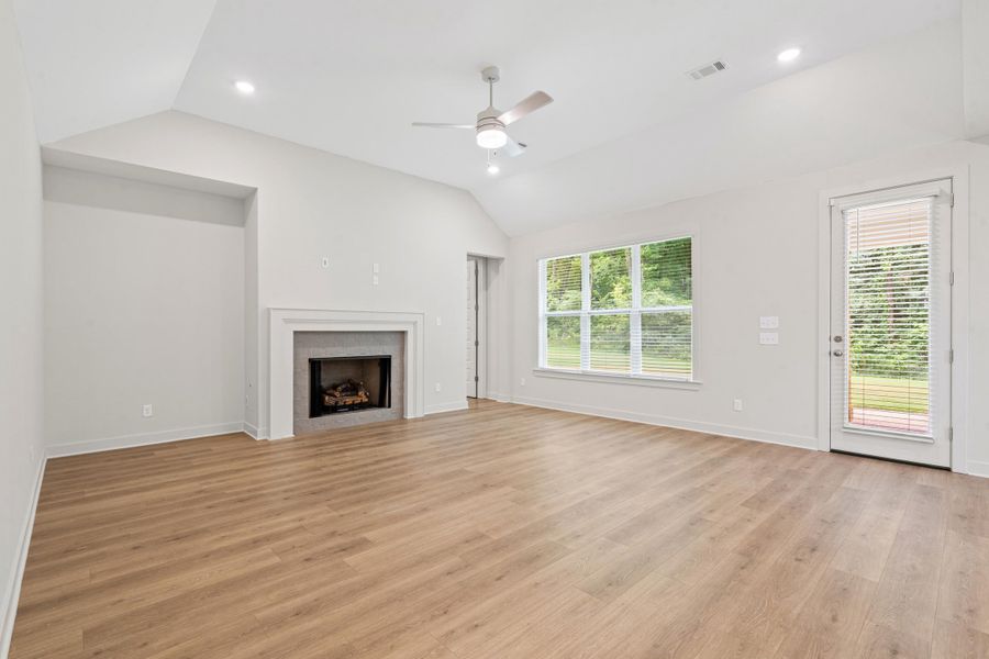 Spacious room featuring vaulted ceilings, wood-finish flooring, a contemporary fireplace with mantel, and a ceiling fan Spacious room featuring vaulted ceilings, wood-finish flooring, a contemporary fireplace with mantel, and a ceiling fan