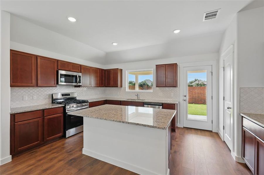 Kitchen featuring stainless steel appliances, decorative backsplash, light stone countertops, dark wood-style flooring, and recessed lighting