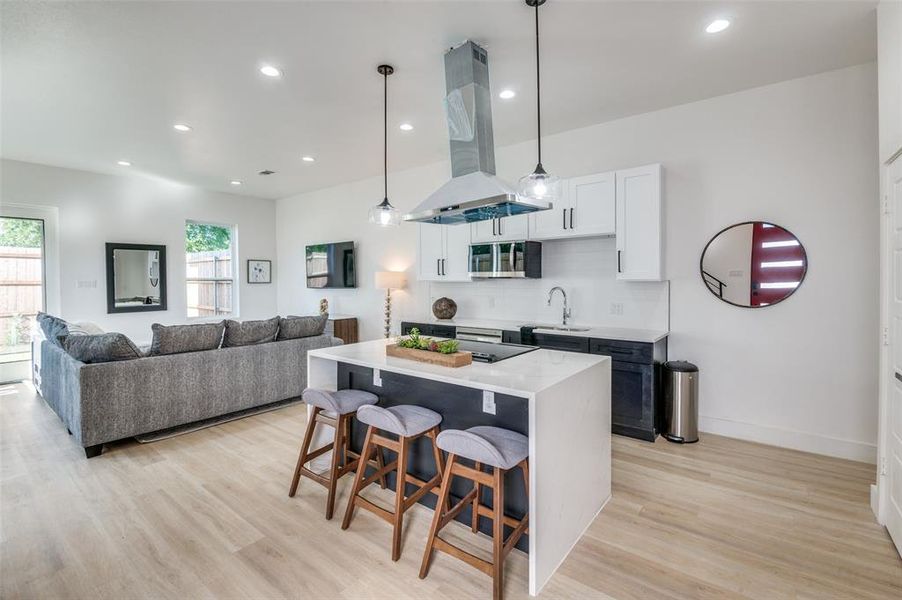 Kitchen with sink, a kitchen island, light wood-type flooring, island exhaust hood, and white cabinetry