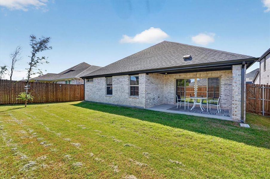 Expansive backyard featuring a covered patio, sliding glass door access, white brick exterior, and a wood privacy fence Expansive backyard featuring a covered patio, sliding glass door access, white brick exterior, and a wood privacy fence
