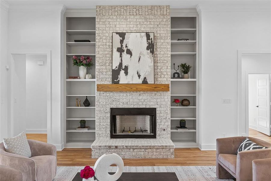 Living area with wood finished floors, built in shelves, crown molding, and a fireplace