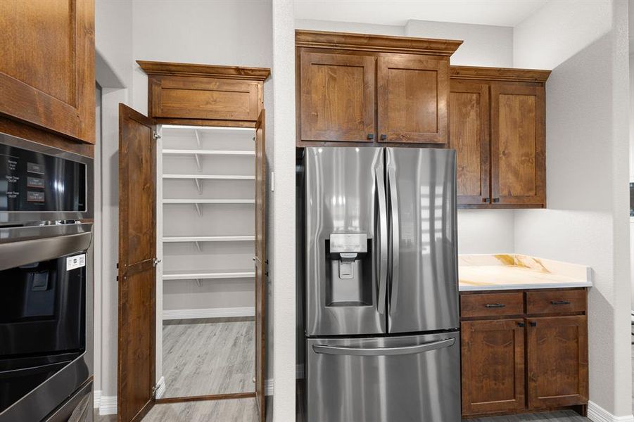 Kitchen featuring stainless steel fridge, light wood-style flooring, light countertops, brown cabinetry, and stainless steel refrigerator