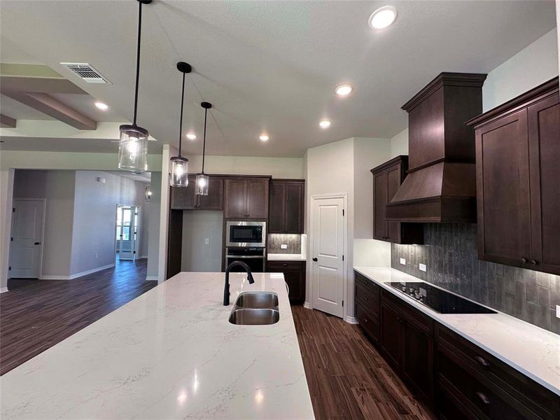 Kitchen featuring dark wood finished floors, hanging light fixtures, light stone countertops, dark brown cabinetry, and stainless steel appliances Kitchen featuring dark wood finished floors, hanging light fixtures, light stone countertops, dark brown cabinetry, and stainless steel appliances