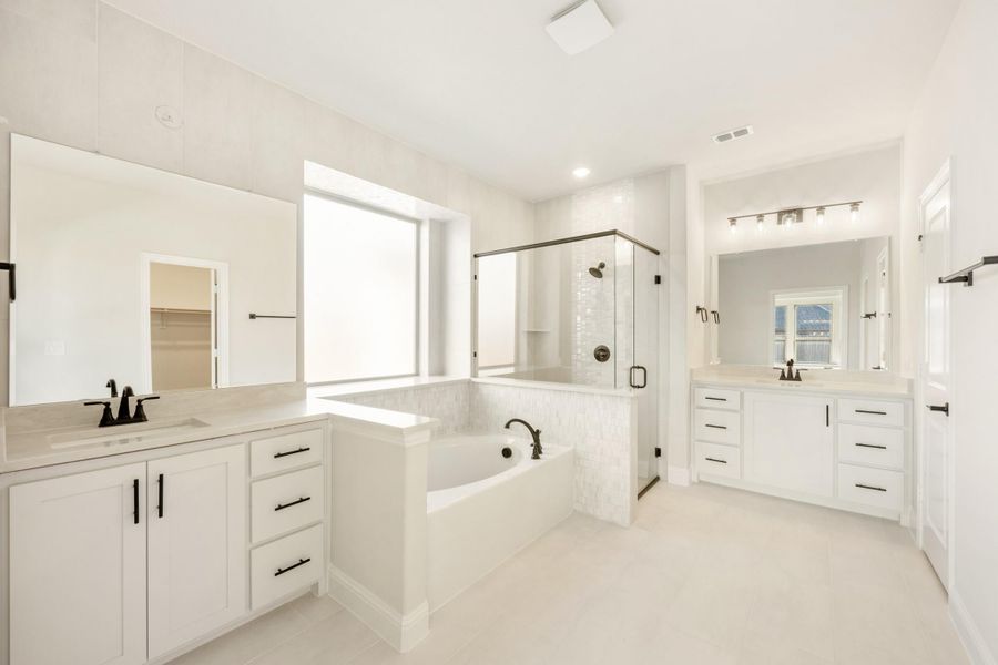 Large master bathroom with dual vanities, soaking tub, and glass walk-in shower with white cabinets and black hardware