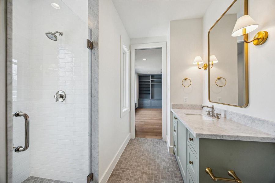 Secondary bath pairs a marble topped vanity in soft sage with warm brass fixtures and an oversized framed mirror for a tailored finish. Subway tile shower with marble trim and mosaic flooring adds classic texture with a fresh, modern edge.
