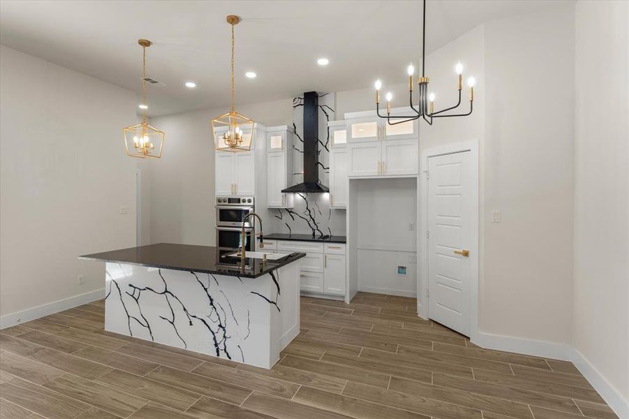 Open Dining, Kitchen, Living area featuring wood tiled floors, hanging lights, white cabinetry, and a kitchen island with sink