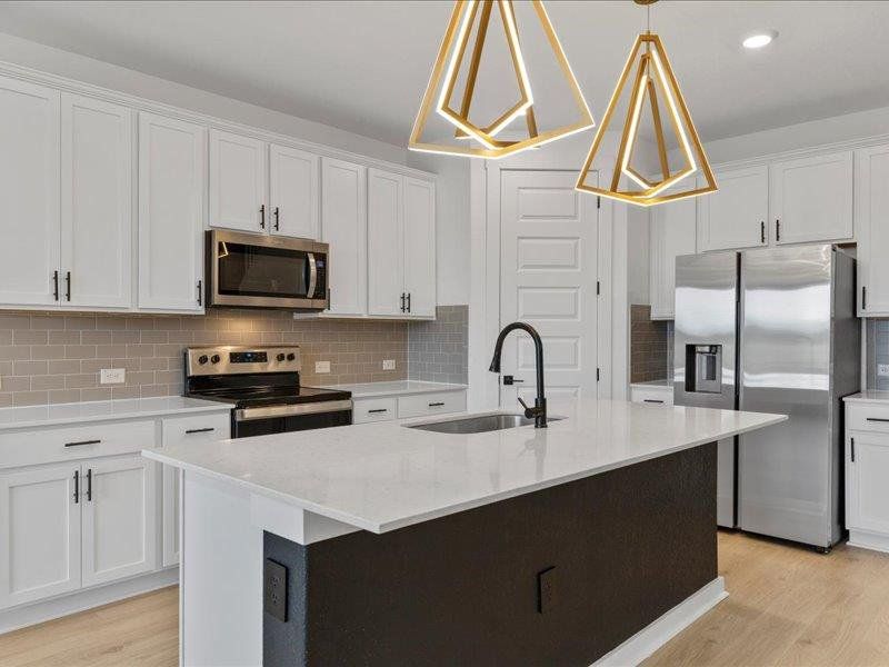 Kitchen featuring appliances with stainless steel finishes, white cabinetry, and a center island with sink