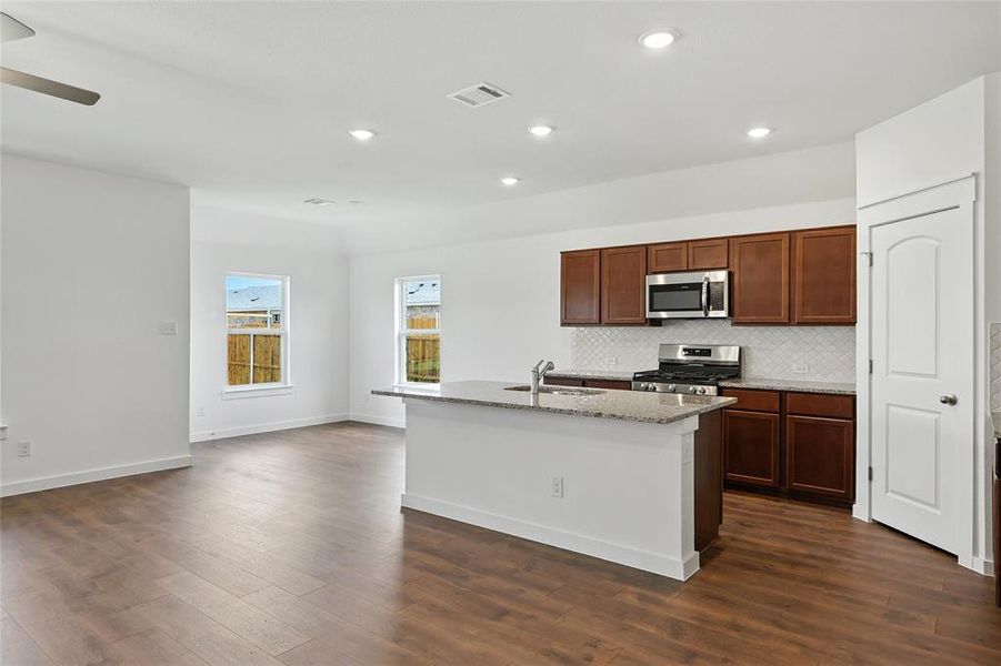 Kitchen with stainless steel appliances, dark wood finished floors, tasteful backsplash, an island with sink, and light stone countertops Kitchen with stainless steel appliances, dark wood finished floors, tasteful backsplash, an island with sink, and light stone countertops