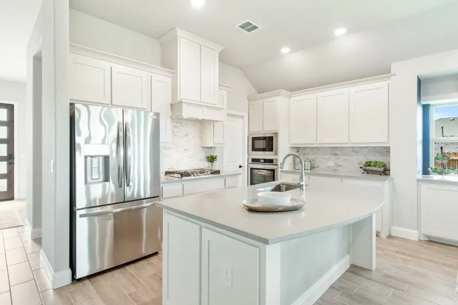 Kitchen with white cabinets, center island with sink, stainless steel appliances, and marble tile backsplash