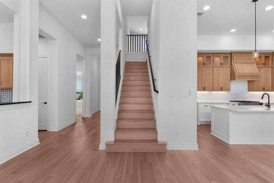 Open concept living space featuring light hardwood flooring, a staircase with black railings, and recessed lighting