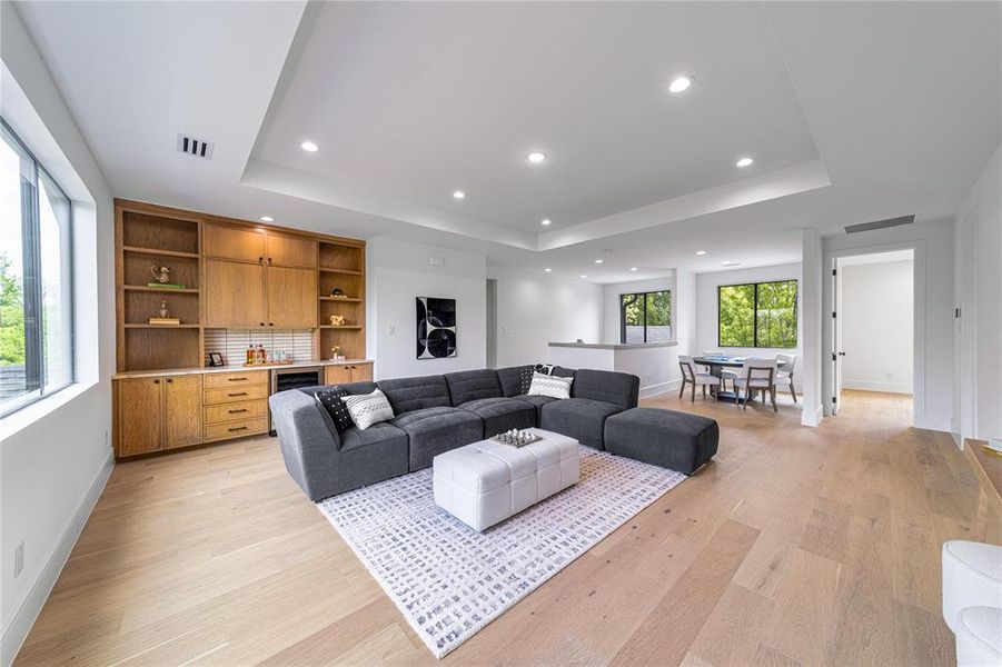 Living room featuring a tray ceiling, light wood-style floors, bar area, recessed lighting, and beverage cooler