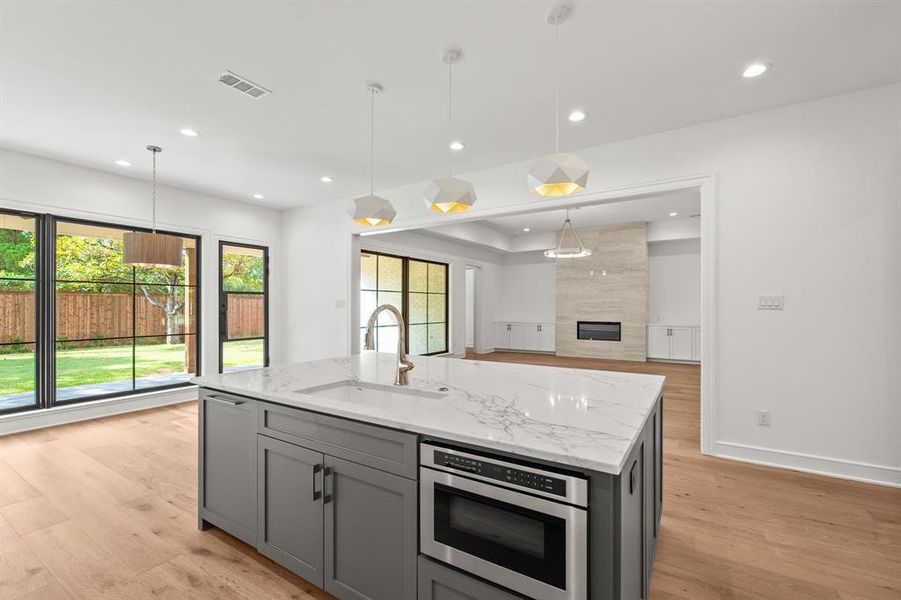 Kitchen with light stone counters, light wood finished floors, a kitchen island with sink, pendant lighting, and recessed lighting Kitchen with light stone counters, light wood finished floors, a kitchen island with sink, pendant lighting, and recessed lighting