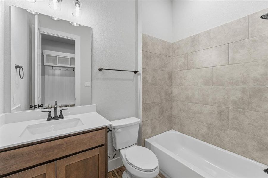 Bathroom featuring a wood-finish vanity with an integrated sink and white countertop, a toilet, a bathtub with a tiled shower surround, and wood-finish flooring