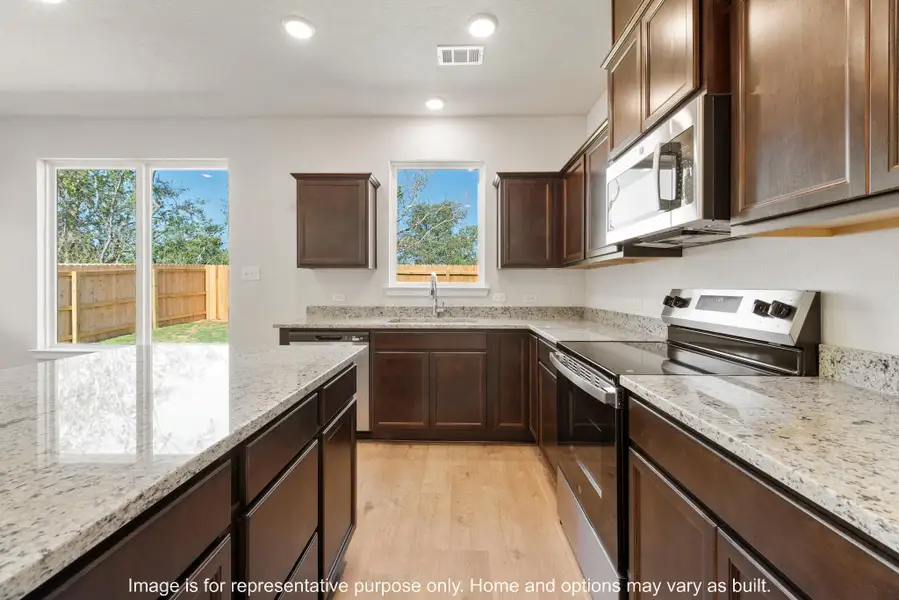 Kitchen with dark wood finish cabinetry, stainless steel appliances, light wood-type flooring, light stone counters, and recessed lighting