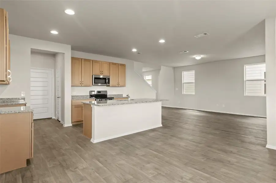Kitchen with appliances with stainless steel finishes, wood finished floors, recessed lighting, open floor plan, and light stone countertops