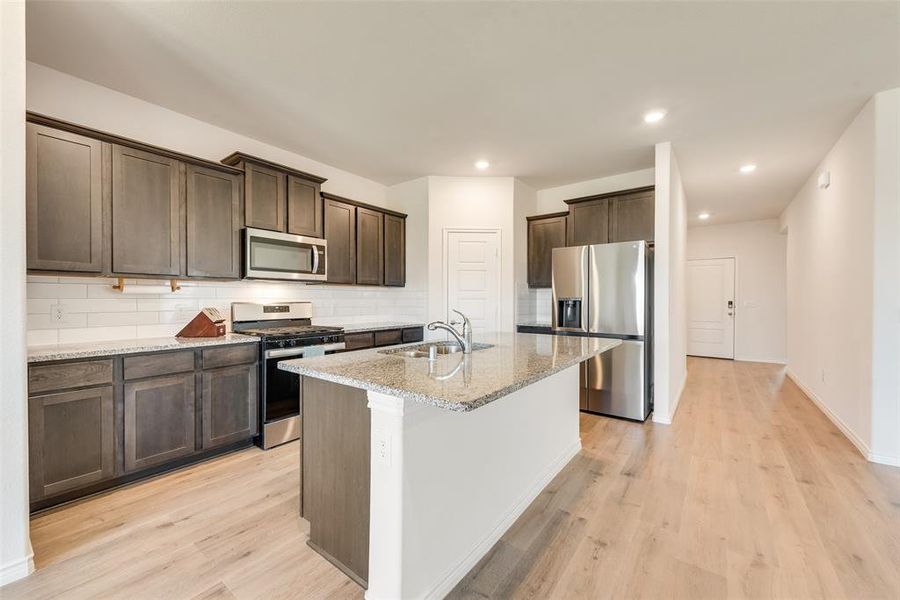 Kitchen featuring dark brown cabinets, stainless steel appliances, open floor plan, light stone countertops, and recessed lighting Kitchen featuring dark brown cabinets, stainless steel appliances, open floor plan, light stone countertops, and recessed lighting