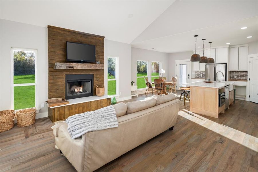 Living room featuring a large fireplace, dark hardwood / wood-style floors, vaulted ceiling, and a healthy amount of sunlight