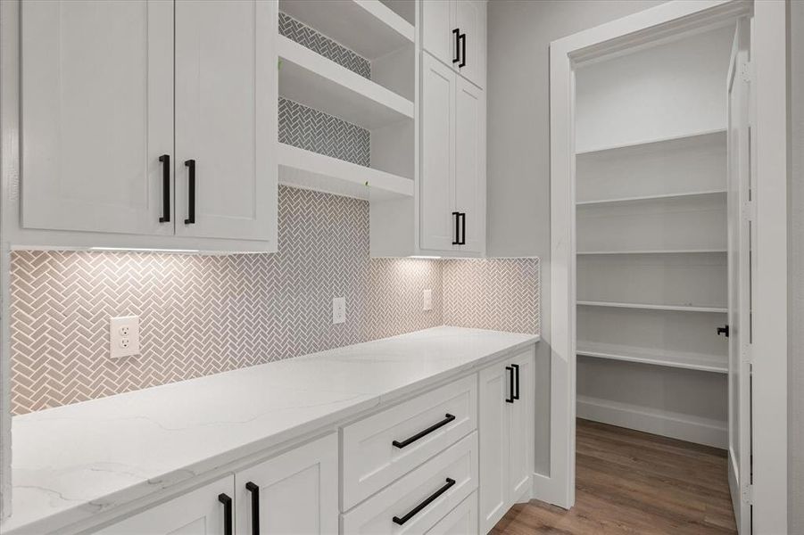Kitchen featuring decorative herringbone backsplash, Calcutta quartz countertops, matte black hardware throughout, pot filler, stainless steal exposed vent hood and waterfall island Kitchen featuring decorative herringbone backsplash, Calcutta quartz countertops, matte black hardware throughout, pot filler, stainless steal exposed vent hood and waterfall island