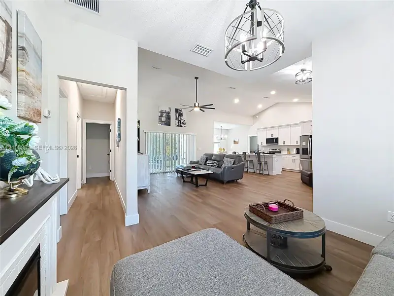 Open-concept interior featuring wood-finish flooring, vaulted ceilings, a metallic cage-style chandelier, white cabinetry, and recessed lighting