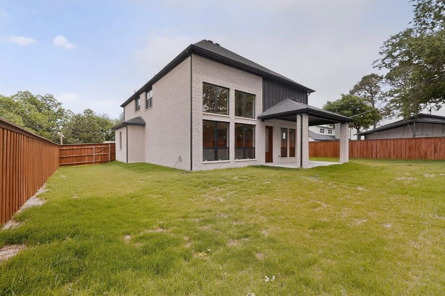 Expansive backyard with a modern two-story home, light brick exterior, dark vertical siding accents, and a covered patio