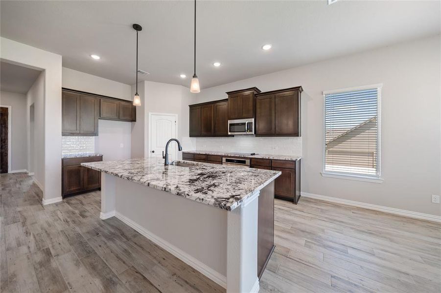 Kitchen featuring backsplash, dark brown cabinetry, recessed lighting, a kitchen island with sink, and decorative light fixtures Kitchen featuring backsplash, dark brown cabinetry, recessed lighting, a kitchen island with sink, and decorative light fixtures