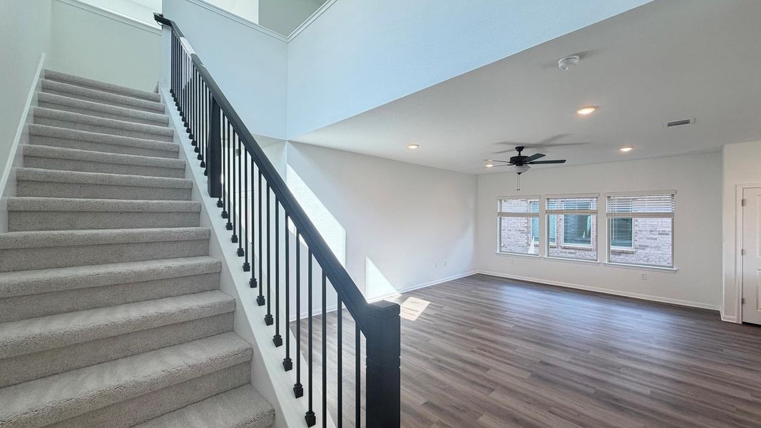 A grand staircase ascends beside an open living area with rich wood flooring and ample natural light. A grand staircase ascends beside an open living area with rich wood flooring and ample natural light.