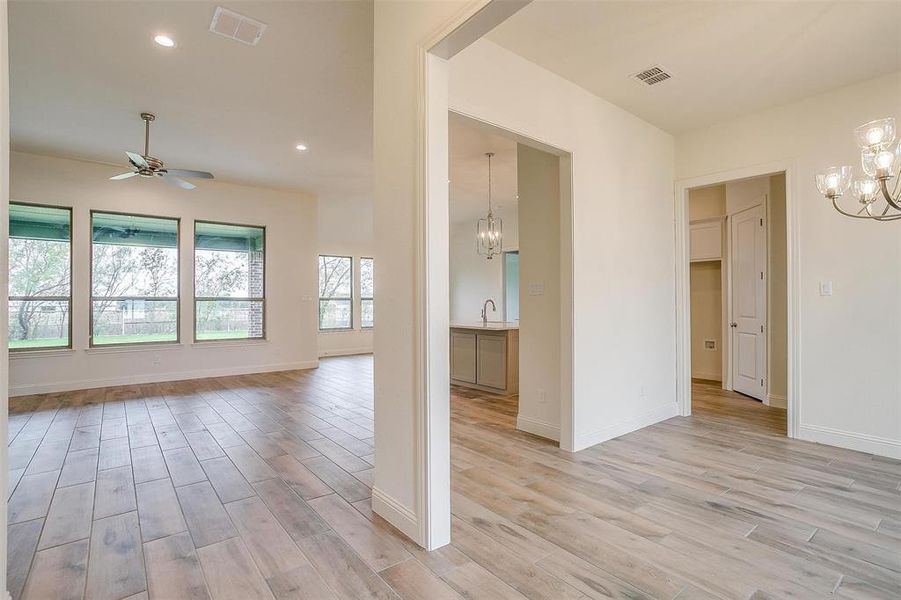 Empty room with light wood-type flooring, ceiling fan with notable chandelier, and sink