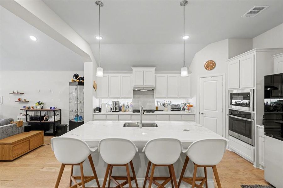 Gourmet kitchen with a large central island, white shaker cabinetry, stainless steel appliances, and pendant lighting