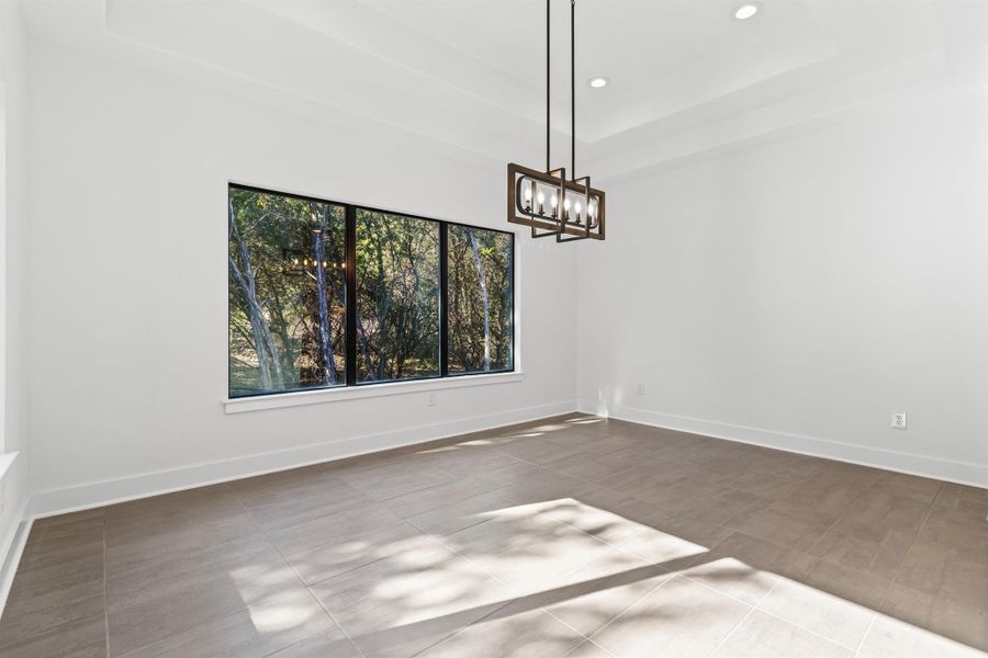 Unfurnished dining area with a raised ceiling, recessed lighting, and a chandelier