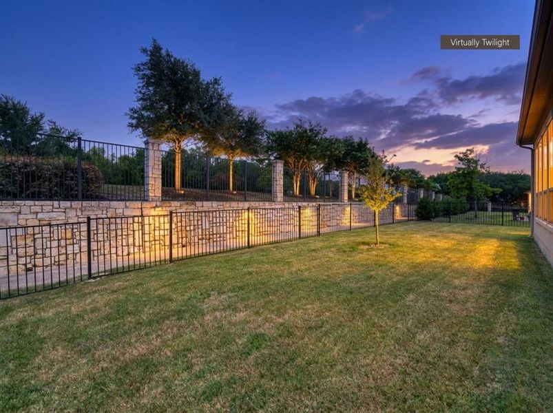 Expansive lawn bordered by a stone retaining wall and black metal fencing