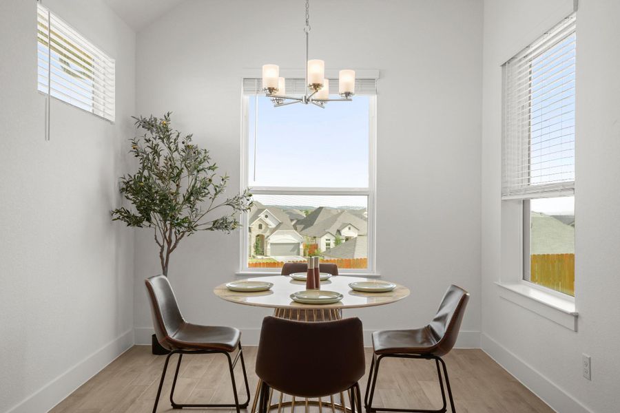A contemporary dining area features warm wood-look flooring and a unique chandelier illuminating a round table, perfect for intimate gatherings.