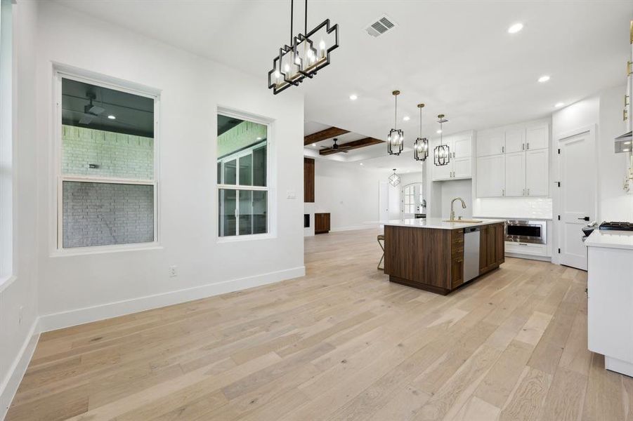 Kitchen with white cabinets, pendant lighting, beam ceiling, a center island with sink, and light hardwood / wood-style flooring