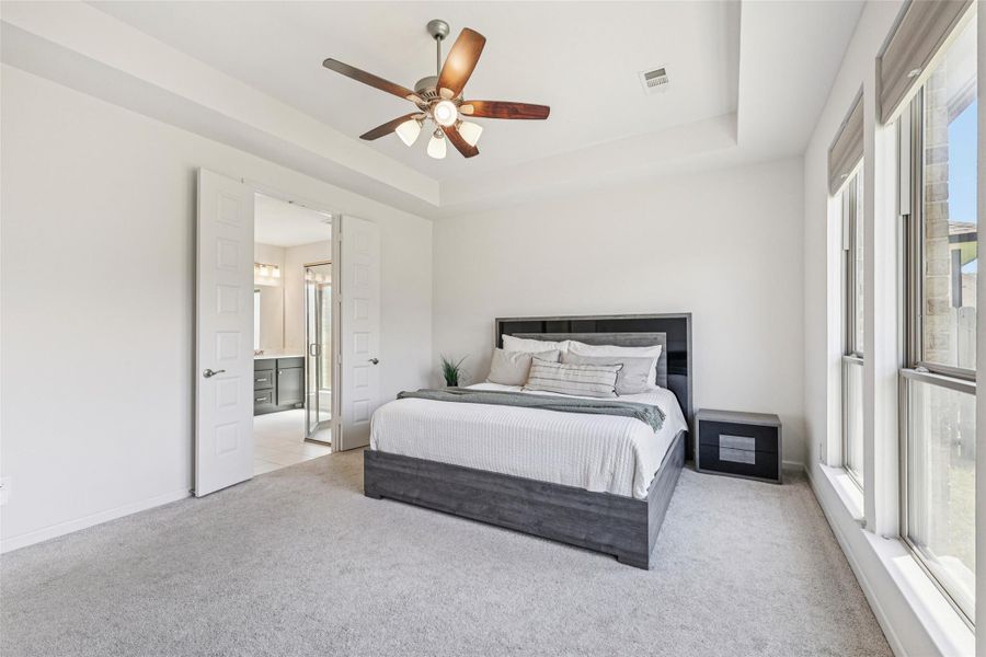 Bedroom featuring light gray carpeting, a tray ceiling with a ceiling fan, and large windows