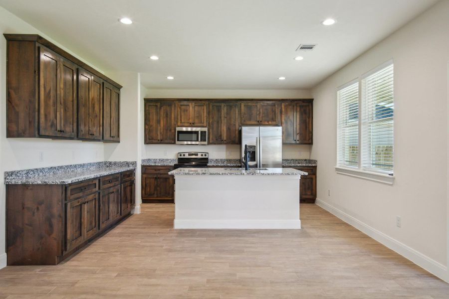 Kitchen with light wood finished floors, recessed lighting, dark brown cabinetry, and appliances with stainless steel finishes Kitchen with light wood finished floors, recessed lighting, dark brown cabinetry, and appliances with stainless steel finishes