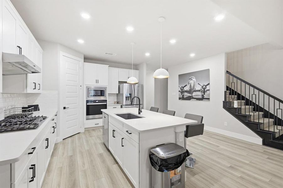 Kitchen with hanging light fixtures, a kitchen breakfast bar, tasteful backsplash, light wood-style flooring, and recessed lighting