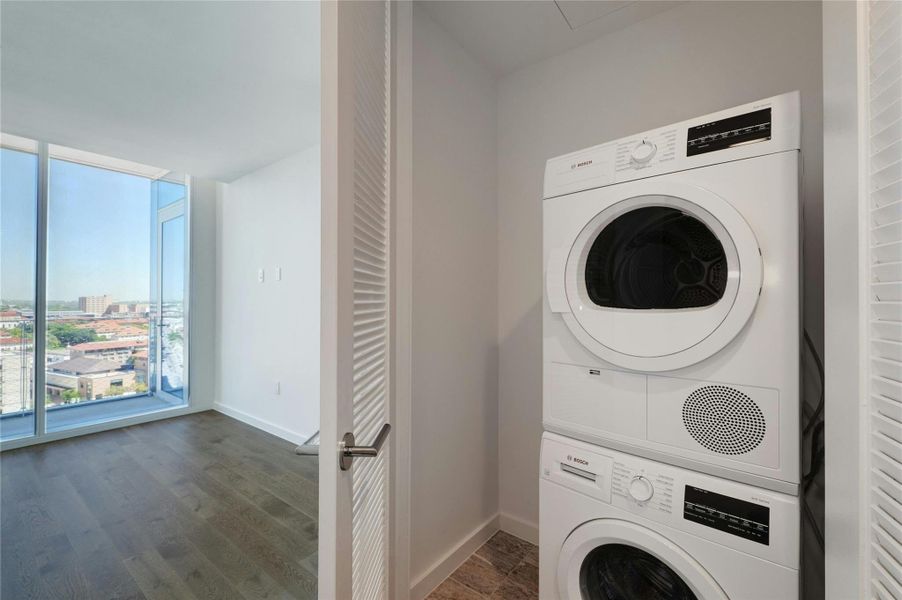 Laundry area with stacked washing machine and dryer and dark wood-style flooring