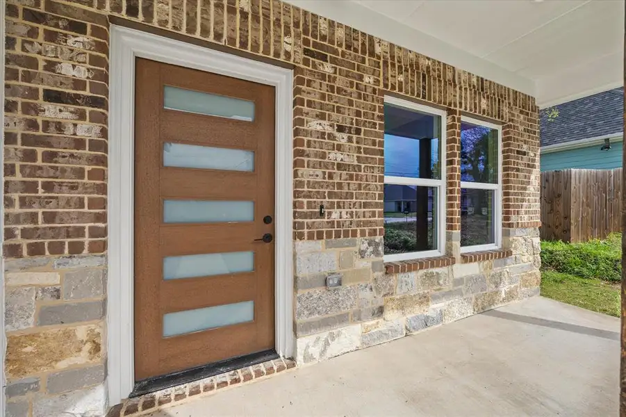 View of exterior entry with a porch, stone siding, and brick siding