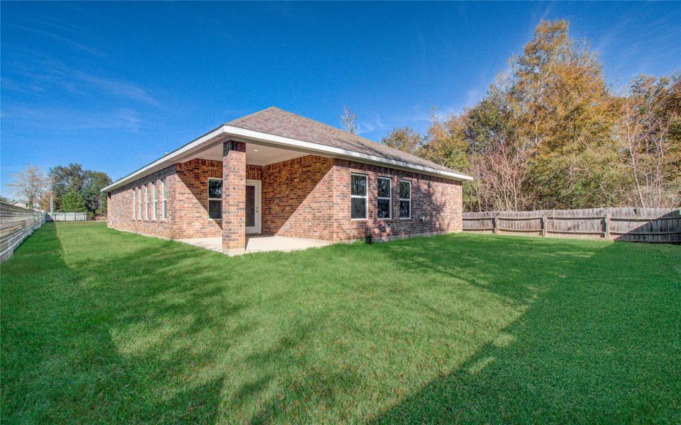 This photo shows a charming brick home with a spacious, well-maintained backyard. It features a covered patio, ideal for outdoor relaxation, and is surrounded by a wooden fence for privacy. The lush green lawn and clear blue sky add to the inviting atmosphere.